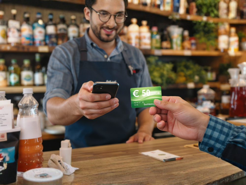 Einlösung eines Arbeitgebergutscheins: Verkäufer scannt eine Sachbezugskarte per Smartphone im regionalen Geschäft